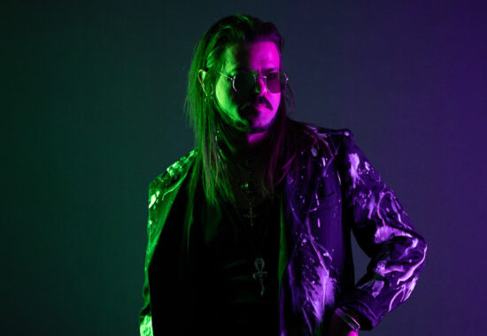 Musician looking away from camera wearing sunglasses with purple and green background