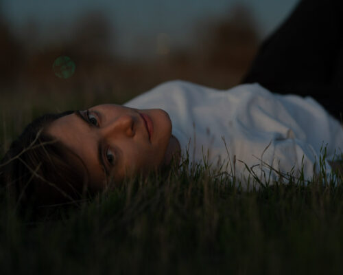 Musician at dusk looking at camera while laying on the grass