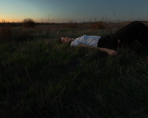 Musician at dusk looking at camera while laying in grass